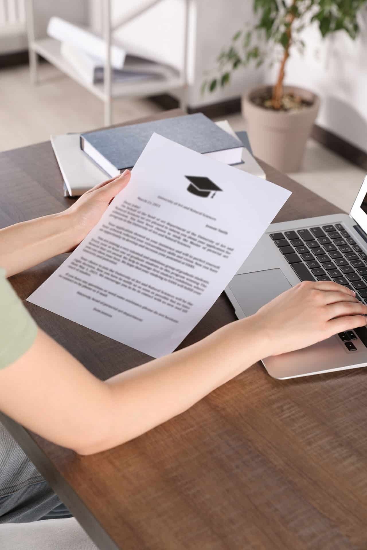 A student at a desk holding a document, reviewing academic qualifications.